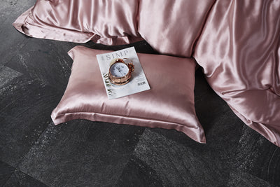 25 momme 100% Silk Pink satin pillow and duvet on a dark surface with a magazine on the pillow.