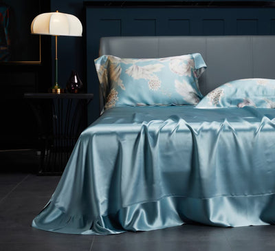 Silk Bedlinen with floral-patterned ocean blue pillows and silk satin sheetsin a dark bedroom setting.